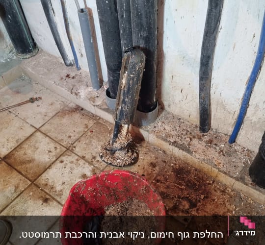 דלי אדום עם פסולת ליד צינורות על רצפה מלוכלכת